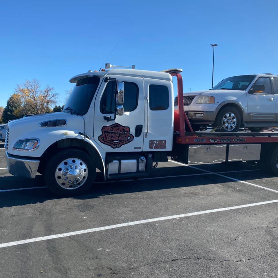 A Giner's Towing flatbed truck transporting a white SUV during the daytime in Aurora, CO.