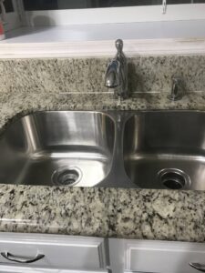A gleaming stainless steel double kitchen sink with a clean granite countertop, showcasing A Clean Xscape LLC's house cleaning in Chandler, AZ.