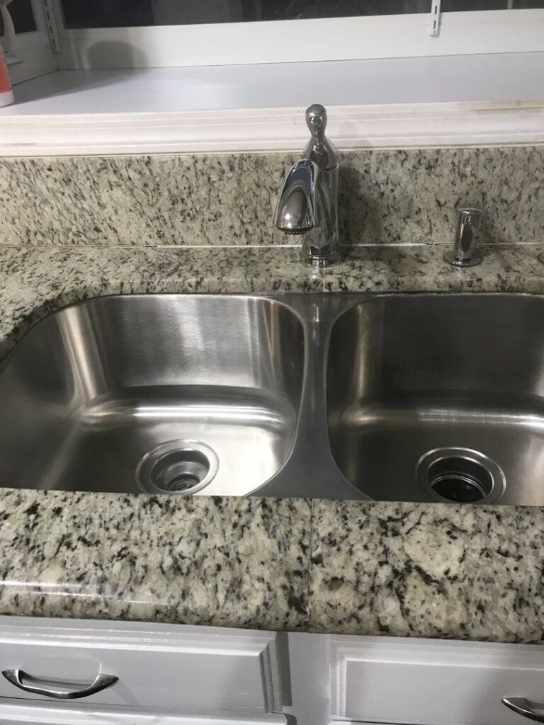 A gleaming stainless steel double kitchen sink with a clean granite countertop, showcasing A Clean Xscape LLC's house cleaning in Chandler, AZ.