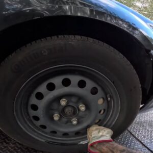 A gloved hand checking a car tire on a flatbed tow truck, part of the service by Columbus Towing in Columbus, GA.