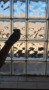 A gloved hand meticulously cleaning glass block windows, demonstrating the detailed work of Jessie Clean in Indianapolis, IN.