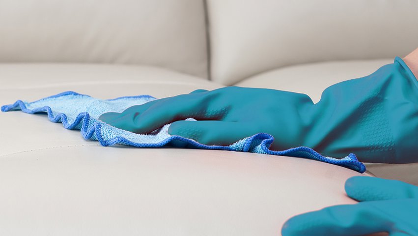 A gloved hand meticulously wiping down a white sofa with a blue microfiber cloth by K & L Cleaning Services in Pelzer, SC.