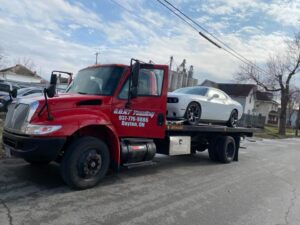 A red flatbed tow truck from Goat Towing transporting a white Dodge Challenger in Dayton, OH.