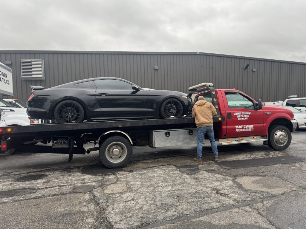 A Goat Towing operator securing a black Ford Mustang onto a flatbed tow truck in Dayton, OH.