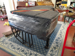 A grand piano carefully wrapped in moving blankets and plastic, ready for transport by All Around Town Movers in Memphis, TN.