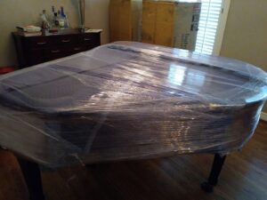A grand piano carefully wrapped in plastic and moving blankets, prepared for transport by Emanuel Movers, Inc. in Houston, TX