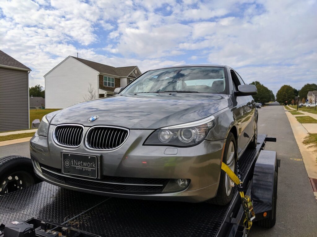 A gray BMW sedan being transported on a car trailer by Snoork Towing in a residential area of Charlotte, NC.