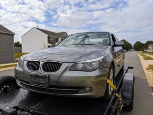 A gray BMW sedan being transported on a car trailer by Snoork Towing in a residential area of Charlotte, NC.
