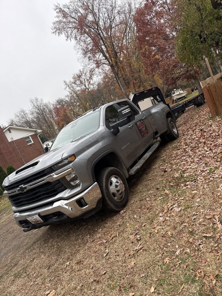 A gray Chevrolet dually pickup truck with a flatbed trailer, ready for towing services from A+1 Towing Service in Middle River, MD.