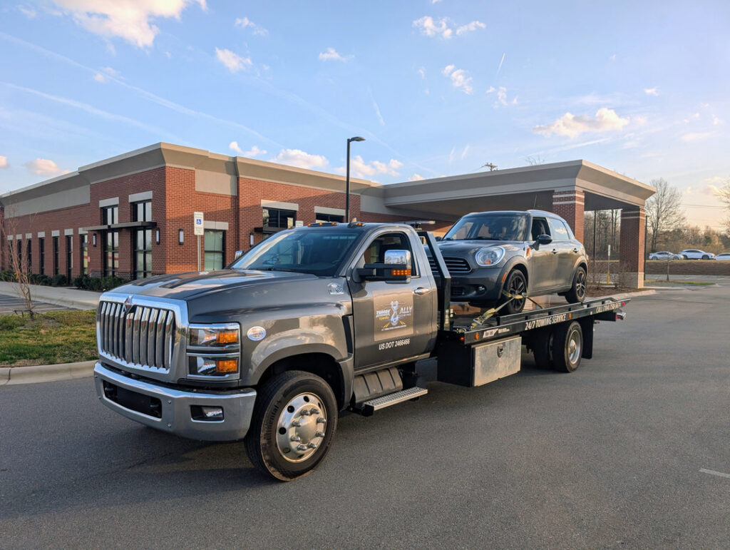 A gray flatbed tow truck from Snoork Towing transporting a dark gray Mini Cooper in Charlotte, NC.