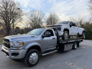 A gray flatbed tow truck from Snoork Towing transporting a white dually pickup truck in Charlotte, NC.