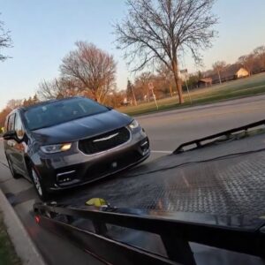 A dark gray minivan being loaded onto a flatbed tow truck for a towing service by Fort Benning Towing in Columbus, GA