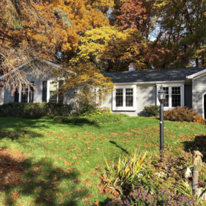 A charming house with gray siding and black shutters, set against autumn foliage, by Exterior Building Products in Indianapolis, IN.
