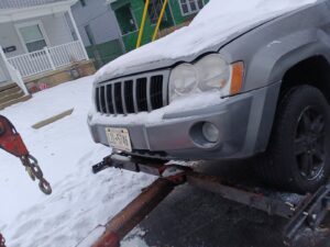 A gray SUV being lifted by a tow truck's wheel lift on a snowy street, performing a towing service by Buffalo Towing Services in Buffalo, NY.