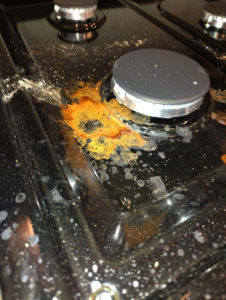 A greasy and dirty stovetop with food spills before cleaning by Carissa's Green Cleaning LLC in Toledo, OH.