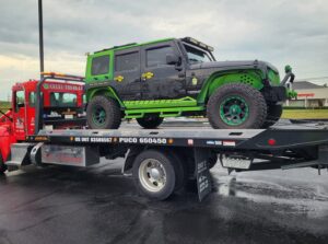 A green and black Jeep being transported on a flatbed tow truck by Vatos Locos Towing in Cincinnati, OH.