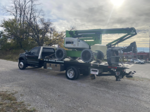 A green boom lift transported on a flatbed tow truck by Triple T's Tow, Tire, & Transportation in Cincinnati, OH.