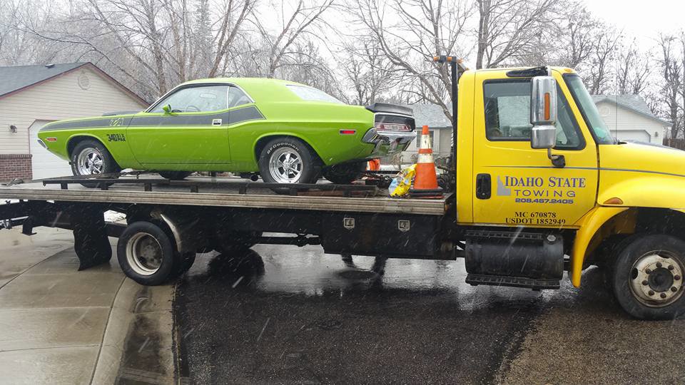 A green classic muscle car being transported on a flatbed tow truck by Idaho State Towing and Recovery in Caldwell, ID.