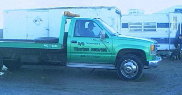 A green flatbed tow truck with 'TOWING SERVICE' written on its side, representing D & S Towing in San Tan Valley, AZ.