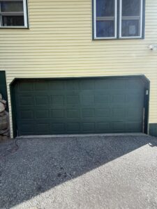 A green garage door installed on a yellow house by Mascolo Overhead Doors & Maintenance in Brookfield, CT.