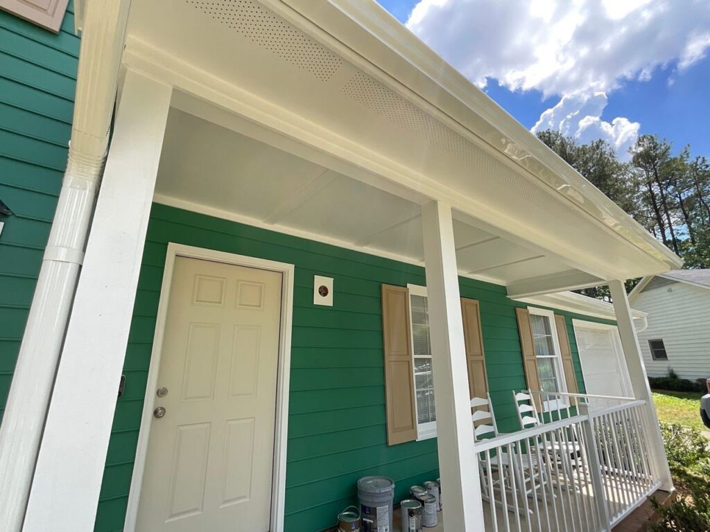 A welcoming front porch of a house with green horizontal siding and white columns by Ideal Siding Winston-Salem, NC.