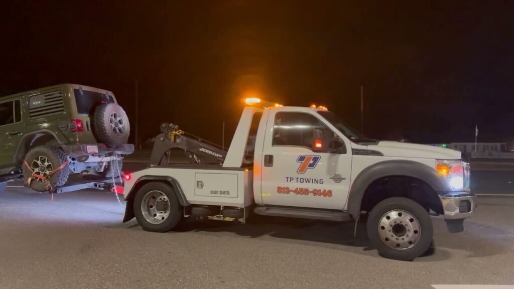 A green Jeep being towed by a TP Towing wheel lift truck at night, providing roadside assistance in Tampa, FL.