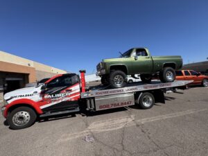 A green lifted pickup truck being transported on a flatbed tow truck by Caliber Towing in Phoenix, AZ.