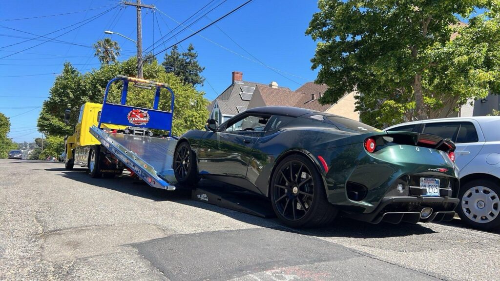 A green Lotus sports car is being loaded onto a flatbed tow truck by S&F Towing in Oakland, CA.