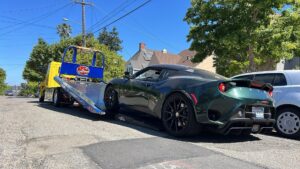 A green Lotus sports car is being loaded onto a flatbed tow truck by S&F Towing in Oakland, CA.
