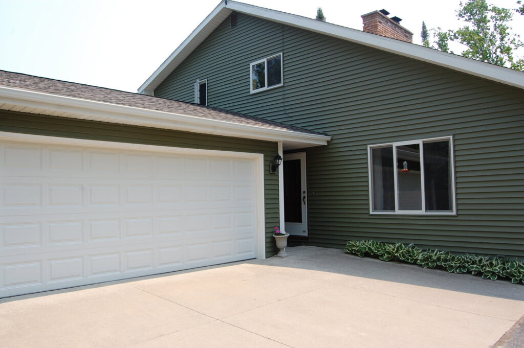 A house with modern green siding and a white garage door, showcasing work by Murphy Builders- Genesee County in Ossineke, MI.