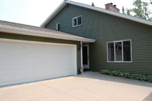 A house with modern green siding and a white garage door, showcasing work by Murphy Builders- Genesee County in Ossineke, MI.