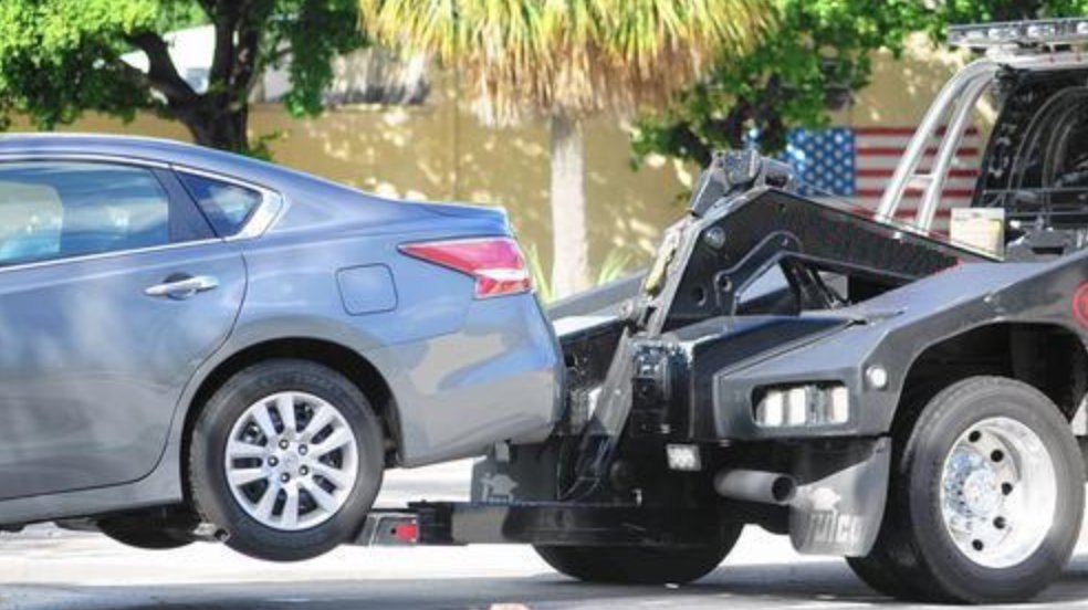 A grey car being towed by a heavy-duty wheel-lift tow truck from Bakersfield Towing Company in Bakersfield, CA.