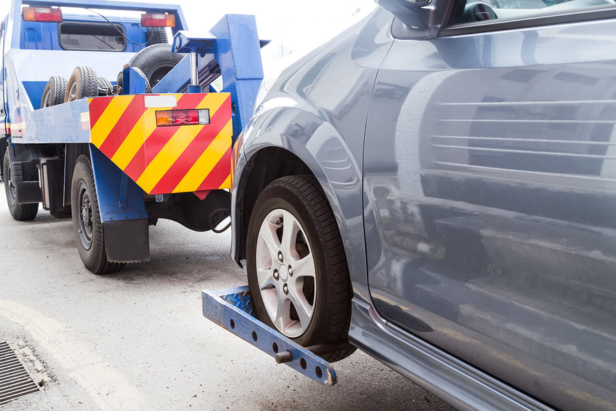 A grey car being towed by a blue wheel-lift tow truck from DunRite Towing Jonesboro in Jonesboro, AR.