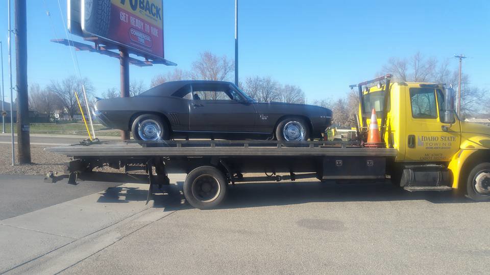 A grey classic muscle car being transported on a flatbed tow truck by Idaho State Towing and Recovery in Caldwell, ID.