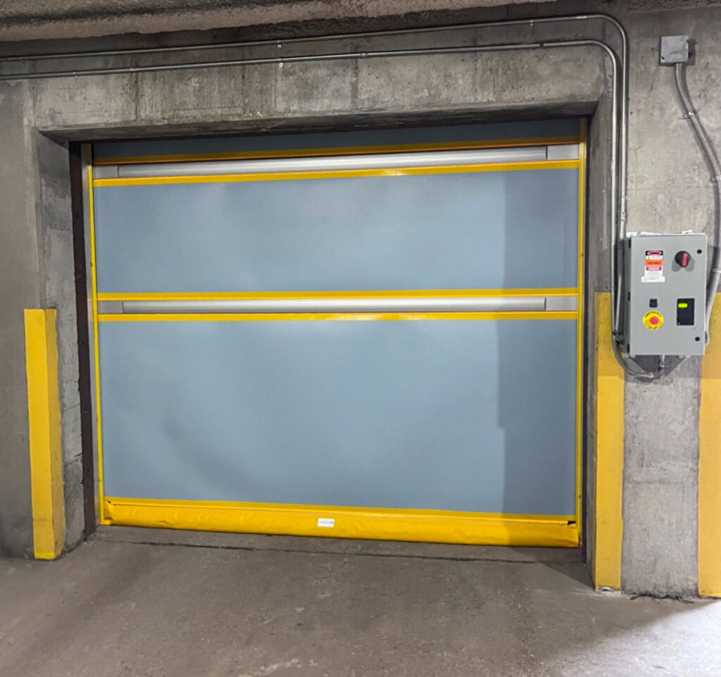 A grey high-speed roll-up door with yellow safety accents, installed by Canyon Overhead Doors in Salt Lake City, UT.