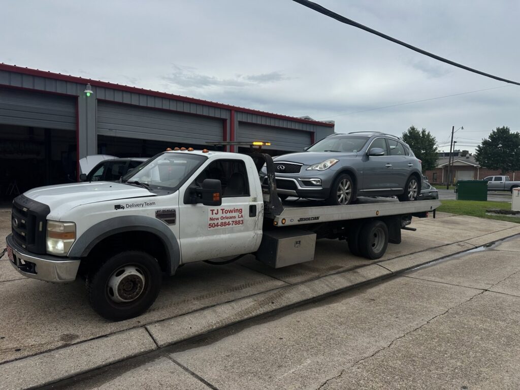 TJ Towing LLC flatbed truck towing a grey Infiniti SUV from a service center in New Orleans, LA.