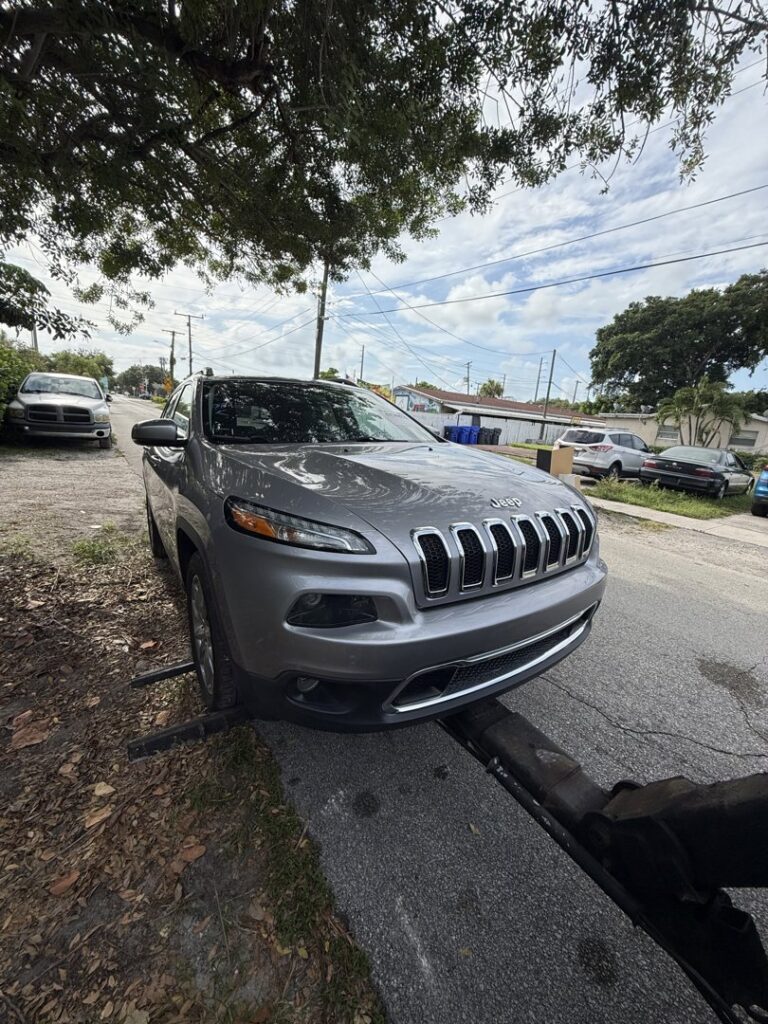 A grey Jeep being towed by a wheel lift tow truck, demonstrating towing services from Cash for junk cars Fort Lauderdale in Fort Lauderdale, FL.