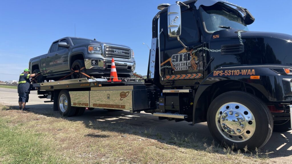 A grey pickup truck being secured onto a flatbed tow truck by a 918 Wrecker Service employee in Tulsa, OK.