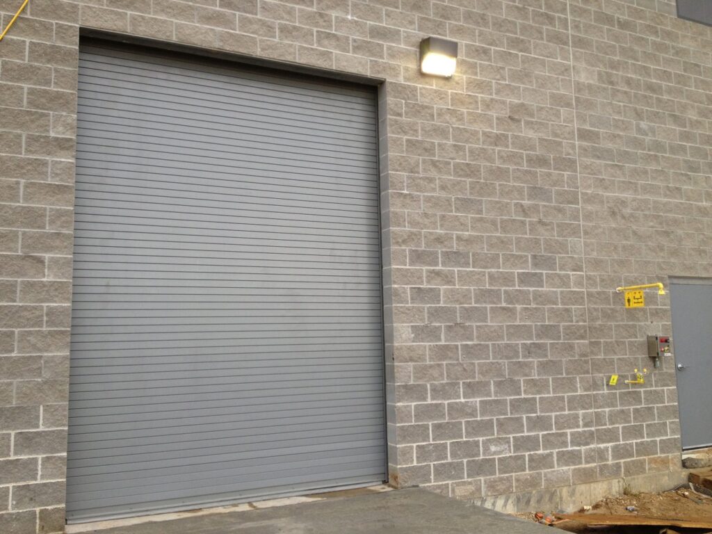 A grey rolling steel commercial garage door installed on a brick building by Alberts Custom Door Company in Wichita, KS.