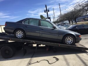 A dark grey sedan being transported on a flatbed tow truck by Bakersfield Towing Company in Bakersfield, CA.