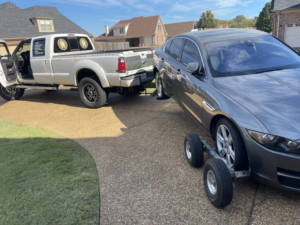 A grey sedan being towed on a tow dolly by a white pickup truck, demonstrating towing services by Swift Response Road Services, LLC in Memphis, TN.