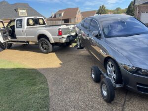 A grey sedan being towed on a tow dolly by a white pickup truck, demonstrating towing services by Swift Response Road Services, LLC in Memphis, TN.