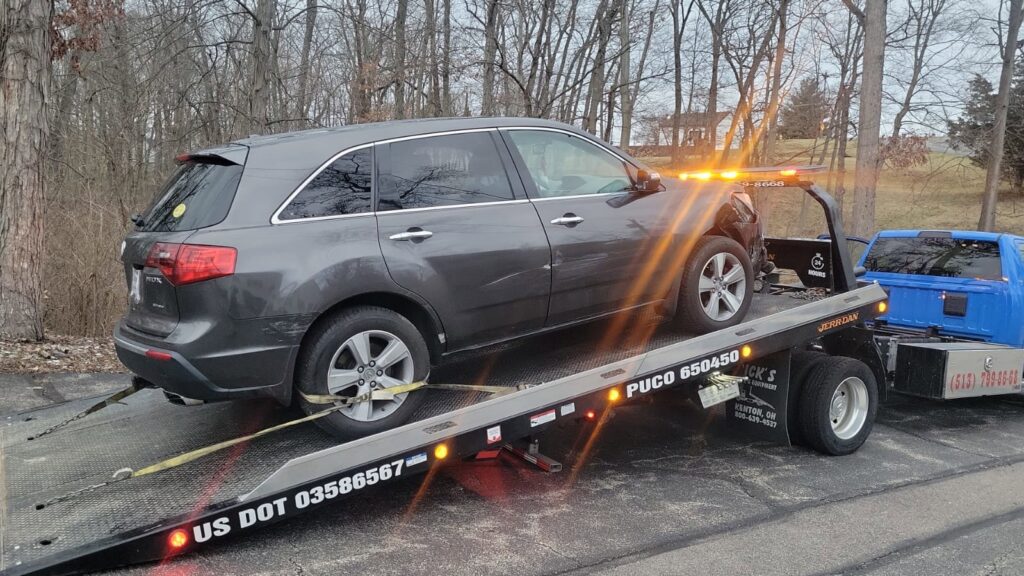 A grey SUV being transported on a flatbed tow truck by Vatos Locos Towing in Cincinnati, OH.