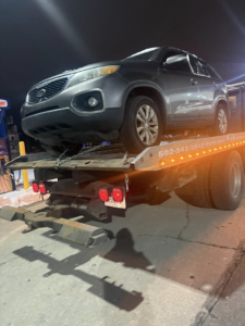 A grey SUV being transported on a flatbed tow truck at night by Tow & go in Louisville, KY.