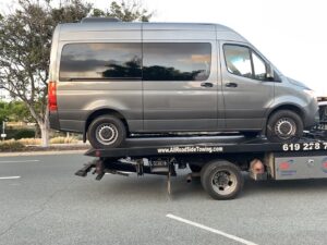 A grey van being transported on a flatbed tow truck by All Roadside Towing San Diego, CA.