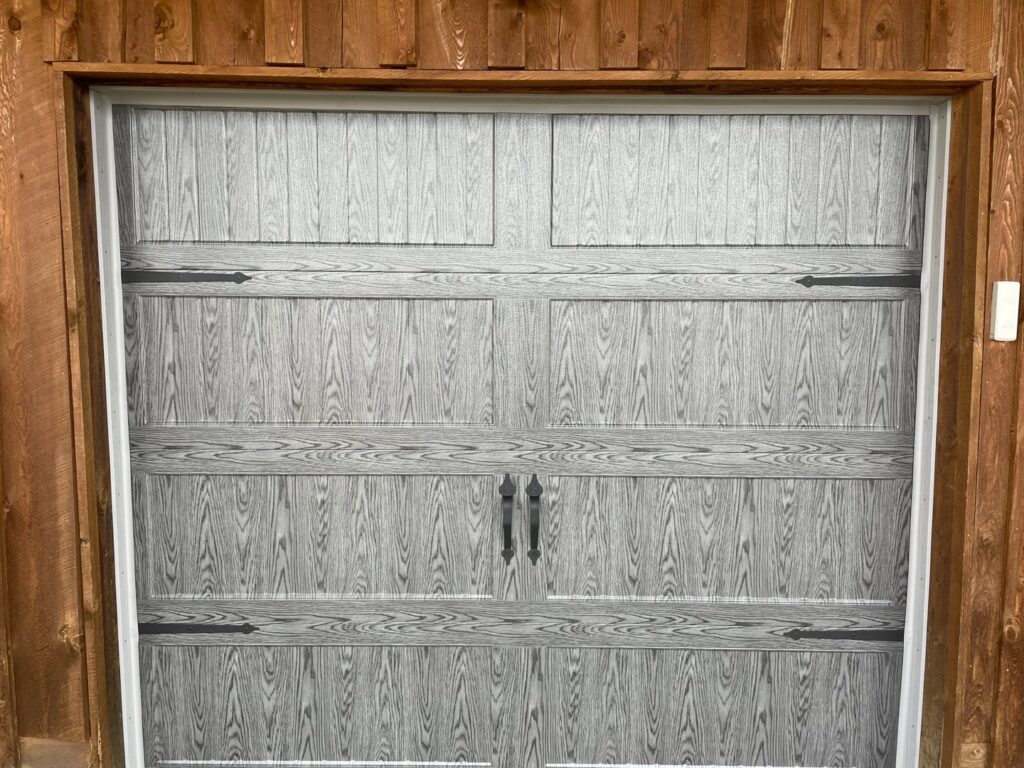 A grey wood-grain style garage door with decorative hardware installed by Elite Garage Door Service & Repair in Billings, MT.