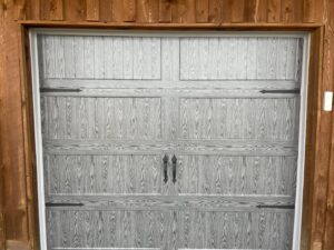 A grey wood-grain style garage door with decorative hardware installed by Elite Garage Door Service & Repair in Billings, MT.