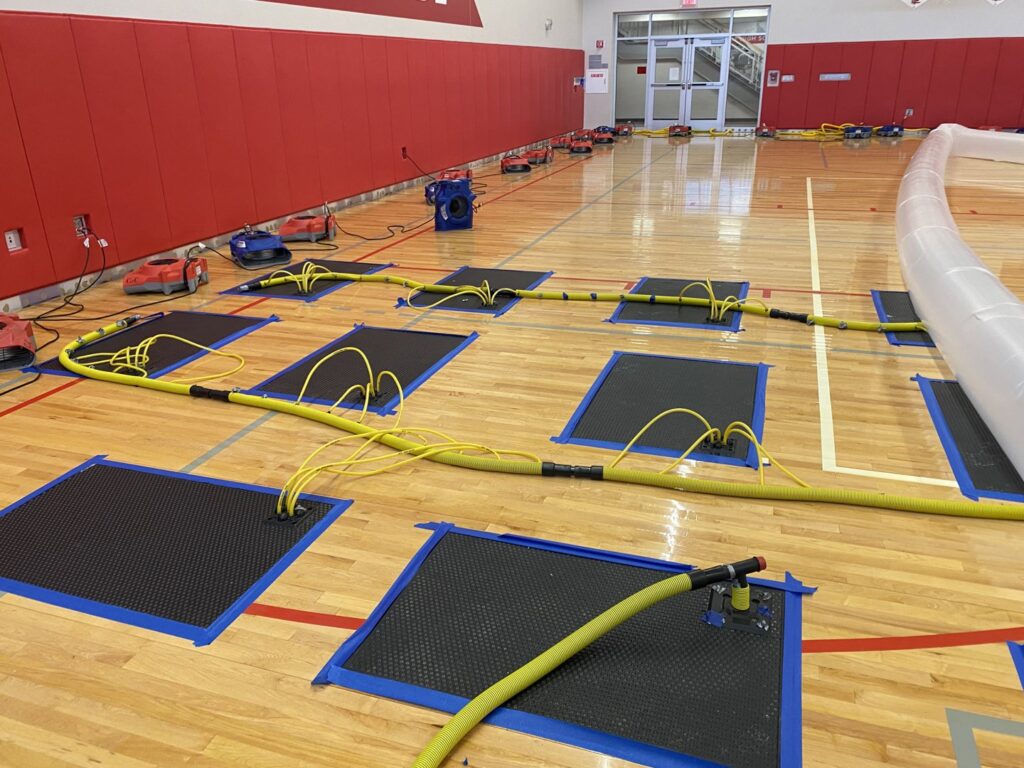 Gymnasium floor with drying mats, hoses, and air movers for water damage restoration by Clean Care of New England in Cranston, RI