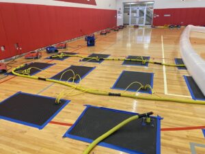 Gymnasium floor with drying mats, hoses, and air movers for water damage restoration by Clean Care of New England in Cranston, RI