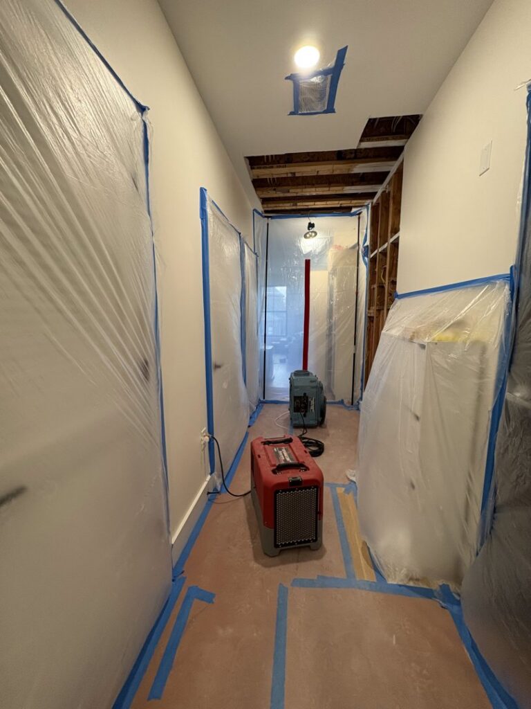 A hallway with plastic containment, exposed ceiling, and drying equipment during water damage restoration by NSH Home Services in Jersey City, NJ.